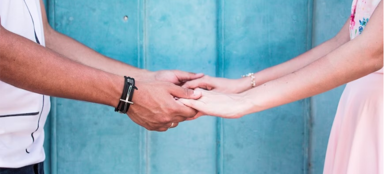 A close-up of a couple holding hands by a blue wall.