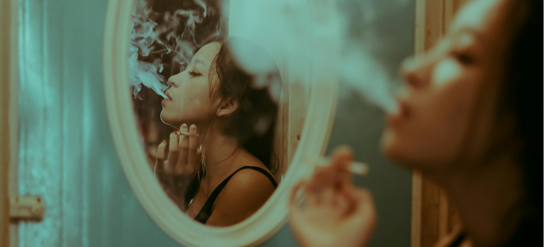 A woman smoking in front of a mirror