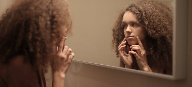 woman checking her skin in the mirror to see how does drug abuse affect skin health.