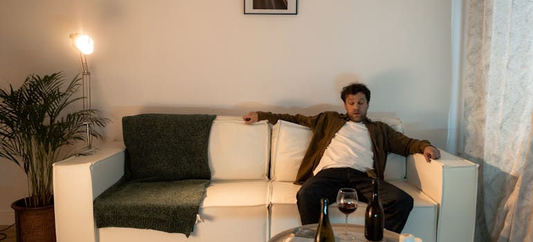 Drunk man sitting on his couch with a wine glass on the coffee table.