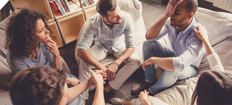A group supporting a friend who is holding his head, ready to get admitted to alcohol addiction treatment center.