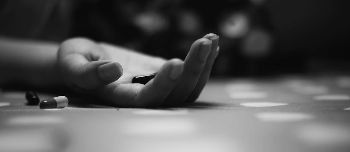 Person's hand on the floor holding a pill.