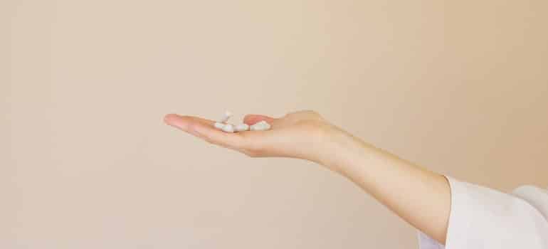 A woman’s extended hand holding white pills.