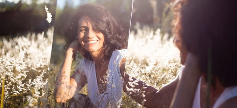A woman outdoors smiling at her reflection in the mirror.