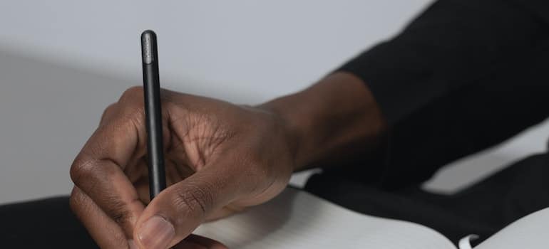 A close-up of a person holding a pen over a notebook.