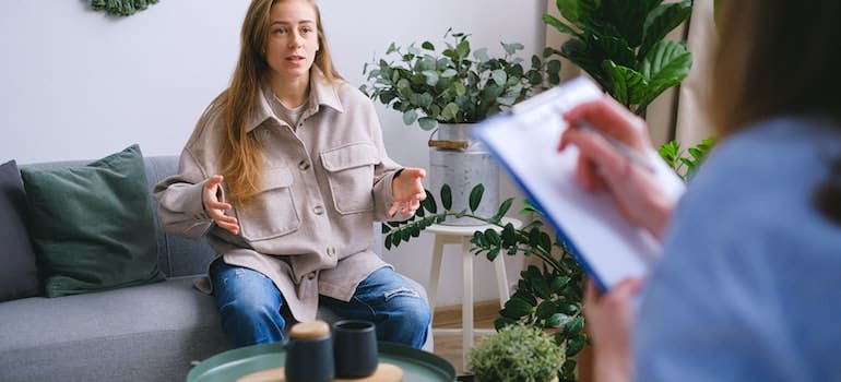 A woman sitting on a couch as her therapist takes notes.