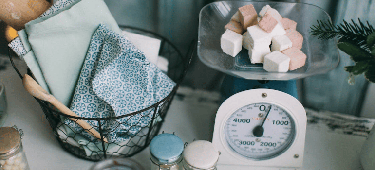 A white kitchen scale weighing sugar cubes and cubes of processed sweets.