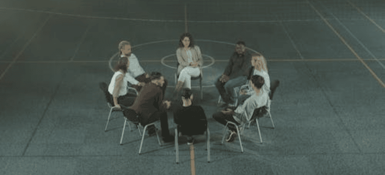 A group of people having a group therapy session in a closed volleyball field.