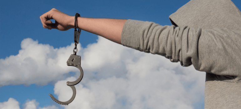 A close-up of a hooded person holding out their hand with one handcuff on.