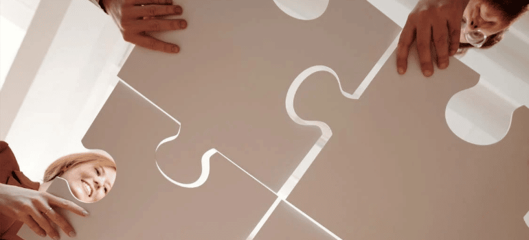 A close-up of people joining together gray puzzle pieces.