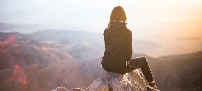 A woman sitting on a mountain peak enjoying the view.