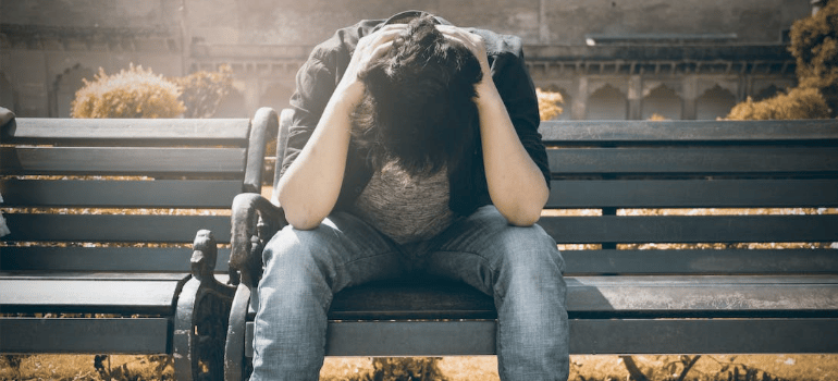 A depressed man sitting on a bench, holding his head in his hands.