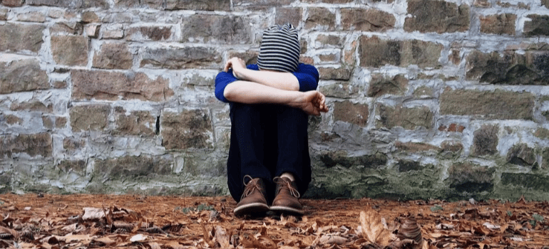 A young man sitting outdoors in a curled position. Depression in recovery