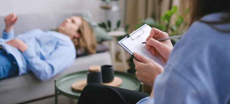 A therapist taking notes as her client lies on the couch.