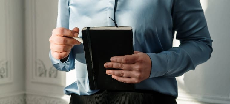 A woman in a blue shirt holding a closed notebook.