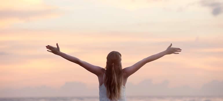 Woman looking at a sky with her arms spread wide in celebration after completing cocaine rehab.