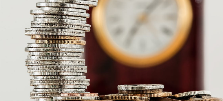 A stack of silver coins in front of a clock.