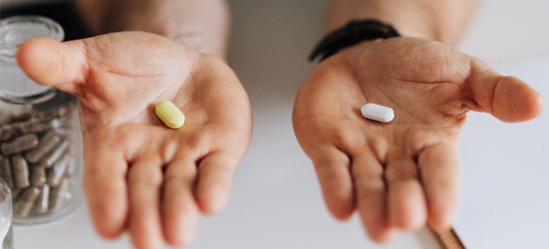 A doctor’s hands, each presenting a pill.