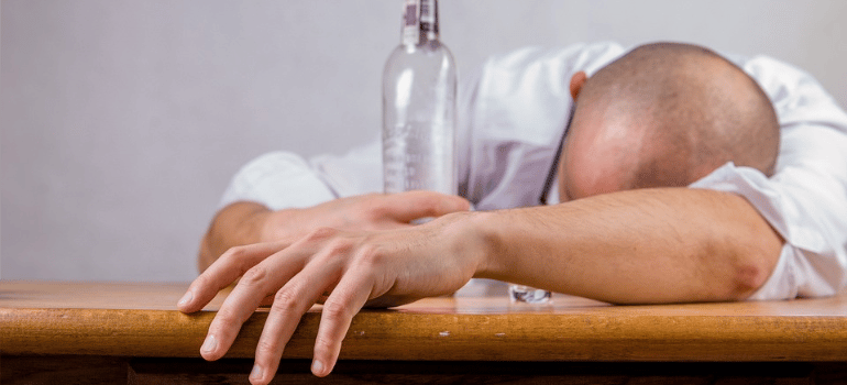 A man lying on a table with a bottle in hand.