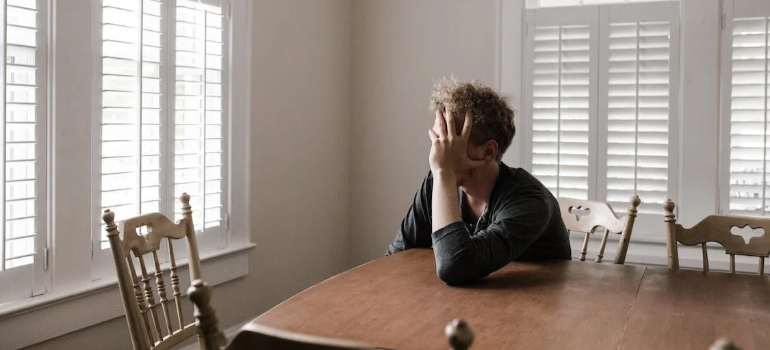 A depressed man leaning on a wooden table indoors.