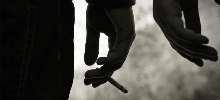A close-up of a young person’s hand holding a cigarette.