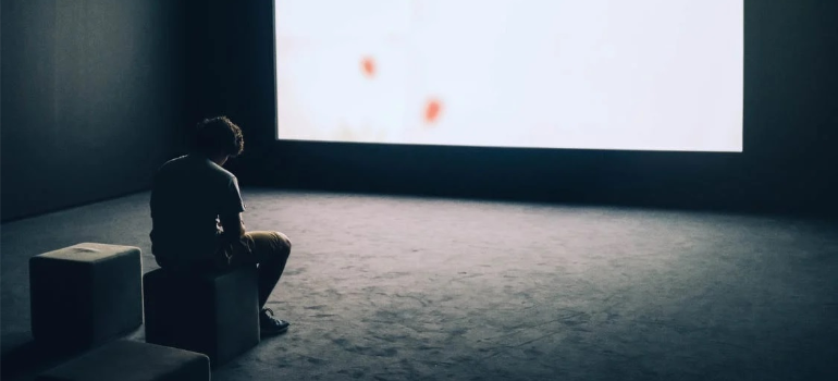 A depressed man sitting in front of a screen indoors.