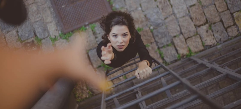 A woman on a ladder stretching her hand to the camera overhead.