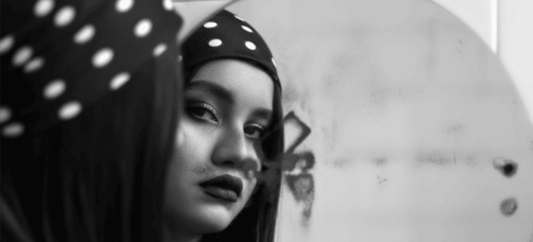 A black-and-white photo of a young woman looking at her reflection in the mirror.