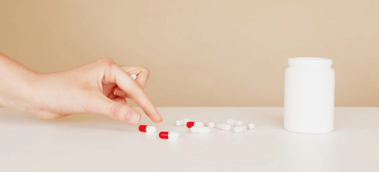 A close-up of a person’s hand picking up a pill from a table.