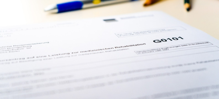 A close-up of a rehab admission document next to a pen and pencils.
