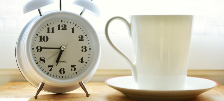 An alarm clock next to a cup on a table.