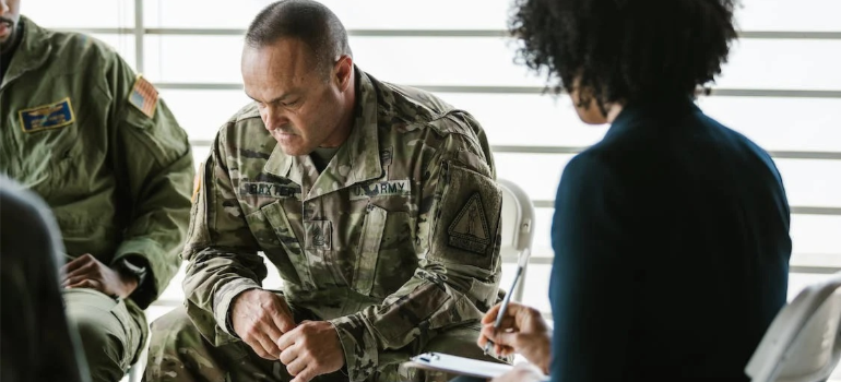 A man in military uniform looking down during a group therapy session indoors.