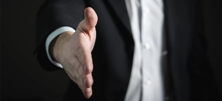 A close-up of a man in a suit extending his hand for a handshake.