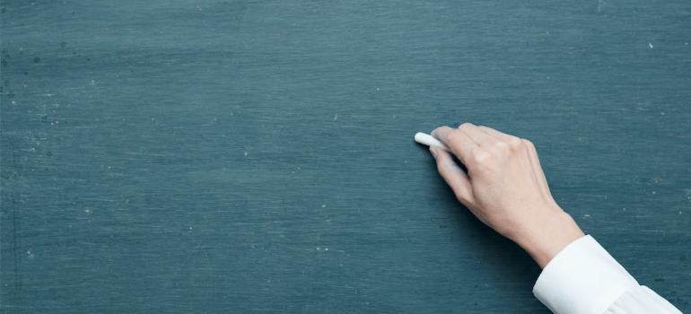 A close-up of a person’s hand holding a white chalk on a blackboard while thinking about alcohol rehab Athens OH