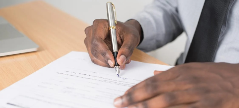 A close-up of a person signing a contract with a pen on a wooden table.