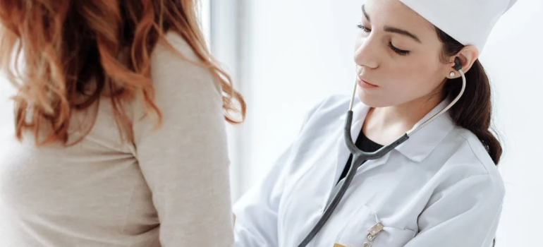 A doctor in a white lab coat with a stethoscope checking on her patient.