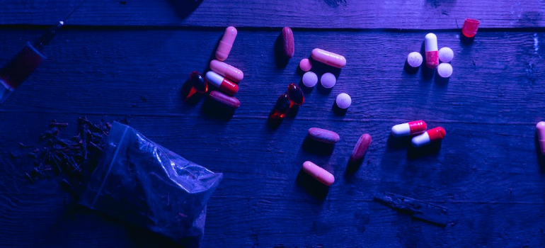 Illicit drug pills and a bag of marijuana on a wooden surface.