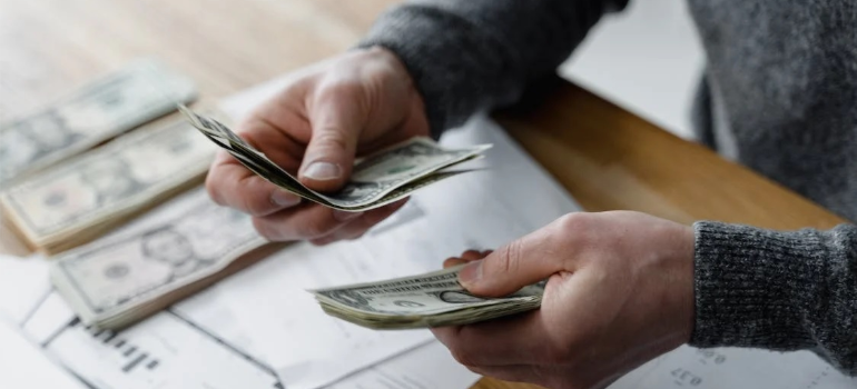 A close-up of a person counting paper money over sheets of paper.