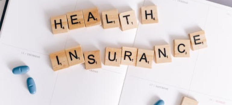 Scrabble tiles on a planner that spell out “health insurance” next to blue pills.