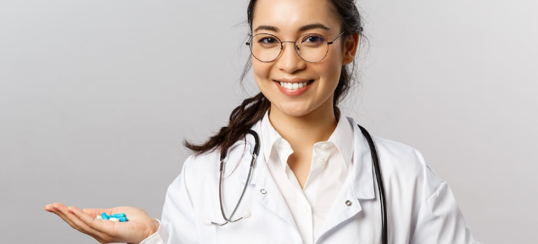 A smiling doctor in a white lab coat holding blue pills.