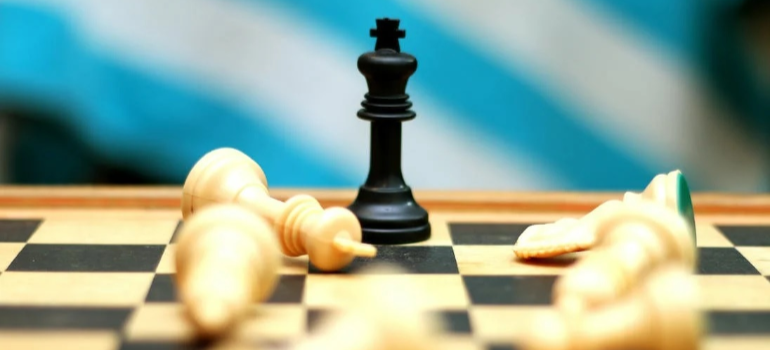 A close-up of a black king chess piece around fallen white pieces.
