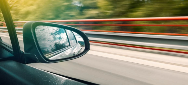 A close-up of a black wing mirror of a driving car.