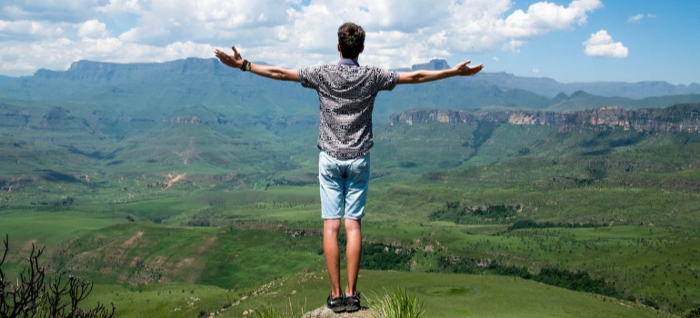 A man in a grey shirt standing on an elevated surface outdoors with open arms after stay in alcohol rehab center Buckhannon WV