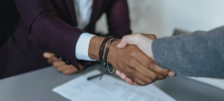 A close-up of two people shaking hands over a sheet of paper on a desk.