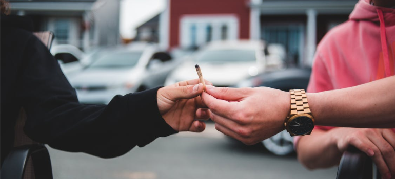 A close-up of two people sharing a cigarette outdoors.