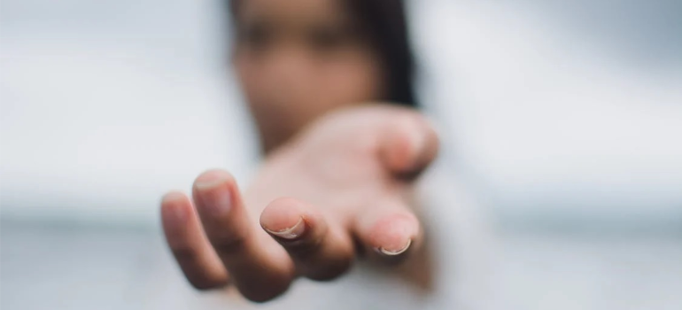 A blurred close-up of a woman’s hand extended toward the camera.
