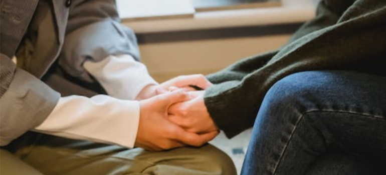 A close-up of a woman holding another woman’s hands to comfort her.