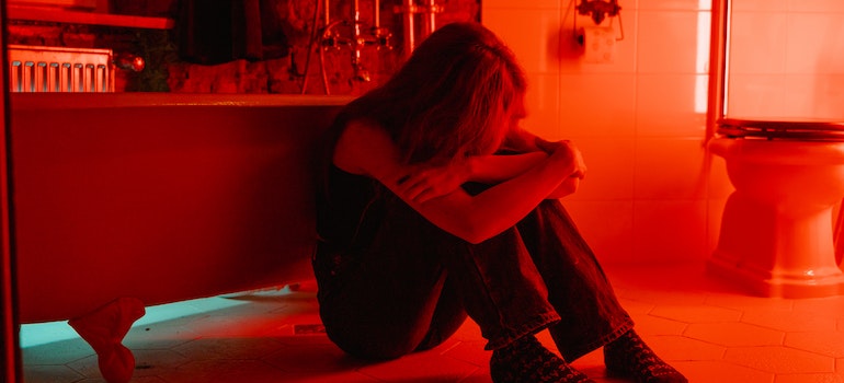 Person on the bathroom floor, hugging their knees.