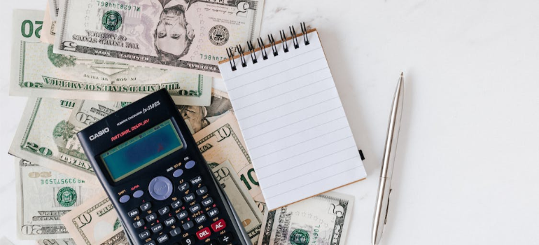 A calculator and a notepad over USD paper bills.