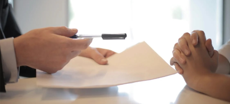 A close-up of a person handing another a pen to sign a contract.